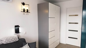 Una habitación moderna con un sofá gris, cojines estampados, una lámpara fijada a la pared, un armario y una puerta.