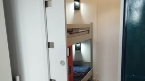 Una habitación compacta con una litera, un escritorio pequeño con lámpara y un armario blanco.
