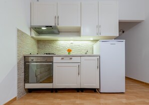 A compact kitchen with white cabinets, a built-in oven, a white refrigerator, and a stone backsplash. - Classy Apartment in the Center of Split (Split)