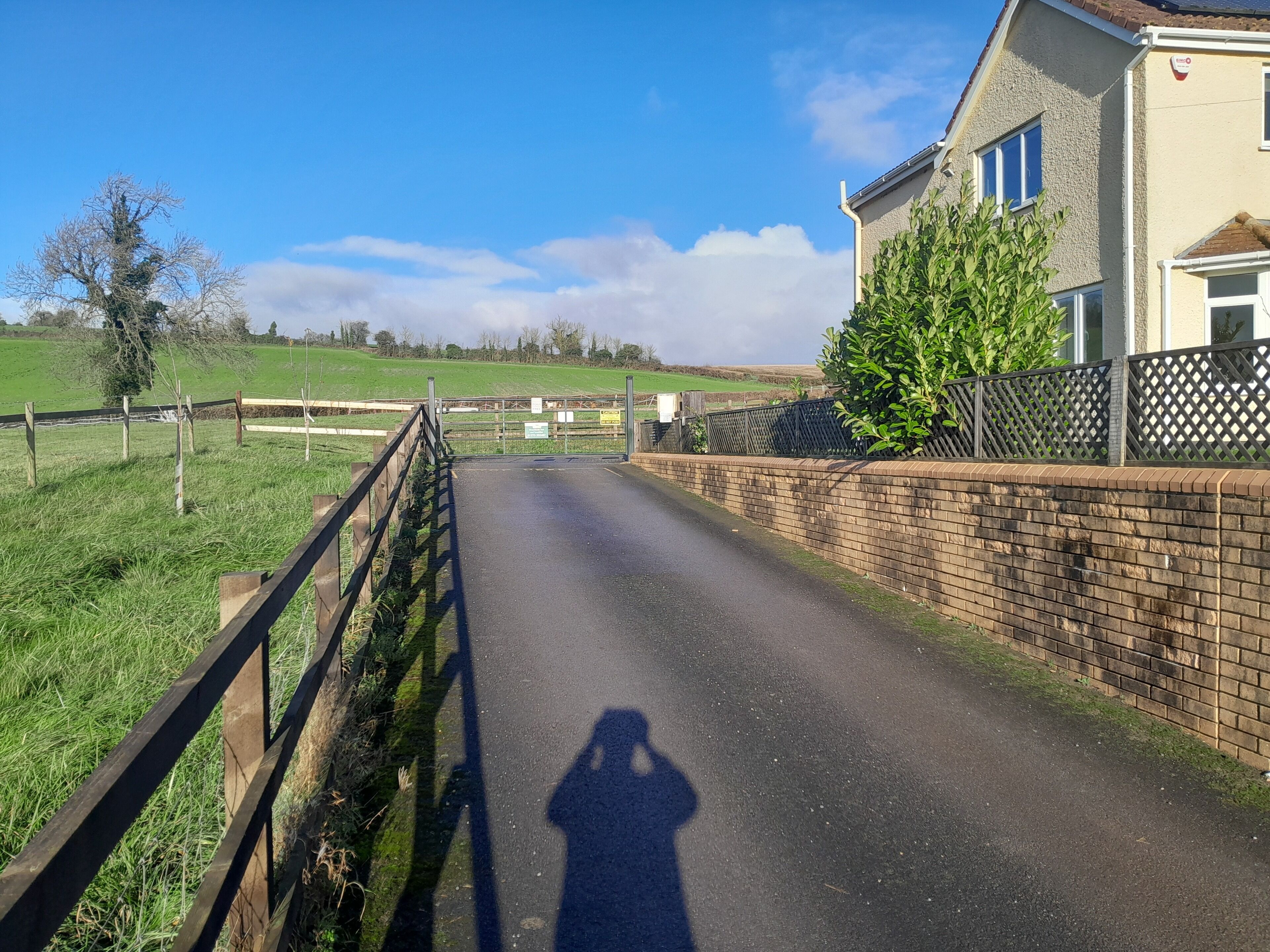 A rural road leading to a house with a brick wall and a wooden fence.