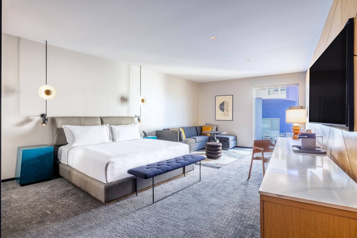 A modern hotel room with a large bed, a desk, a chair, and a view of the outside.