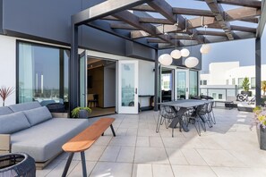 An outdoor patio with a sofa, table, chairs, and hanging lights. - The Shay Hotel (Culver City)
