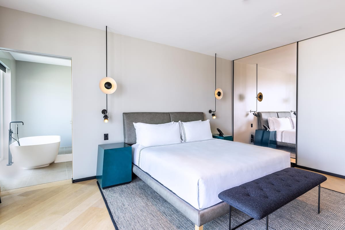 A modern hotel room with a large bed, a bathtub, and a large mirror.