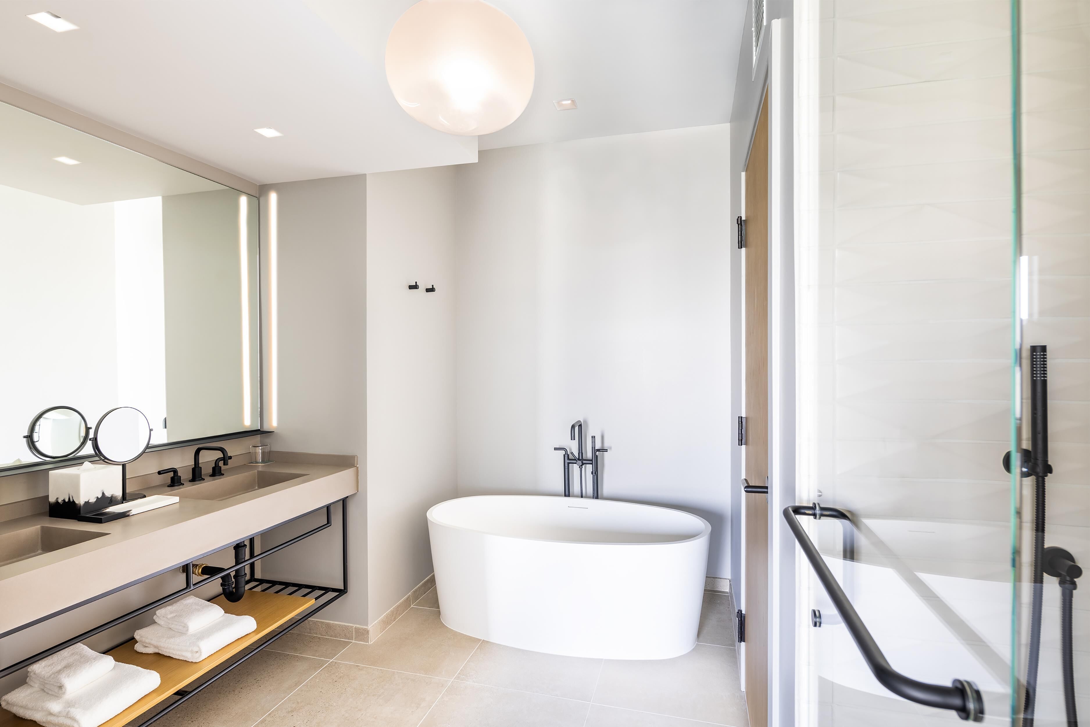 Ein modernes Badezimmer mit einer großen Badewanne, einem Waschtisch mit Spiegel und einer Duschkabine aus Glas.