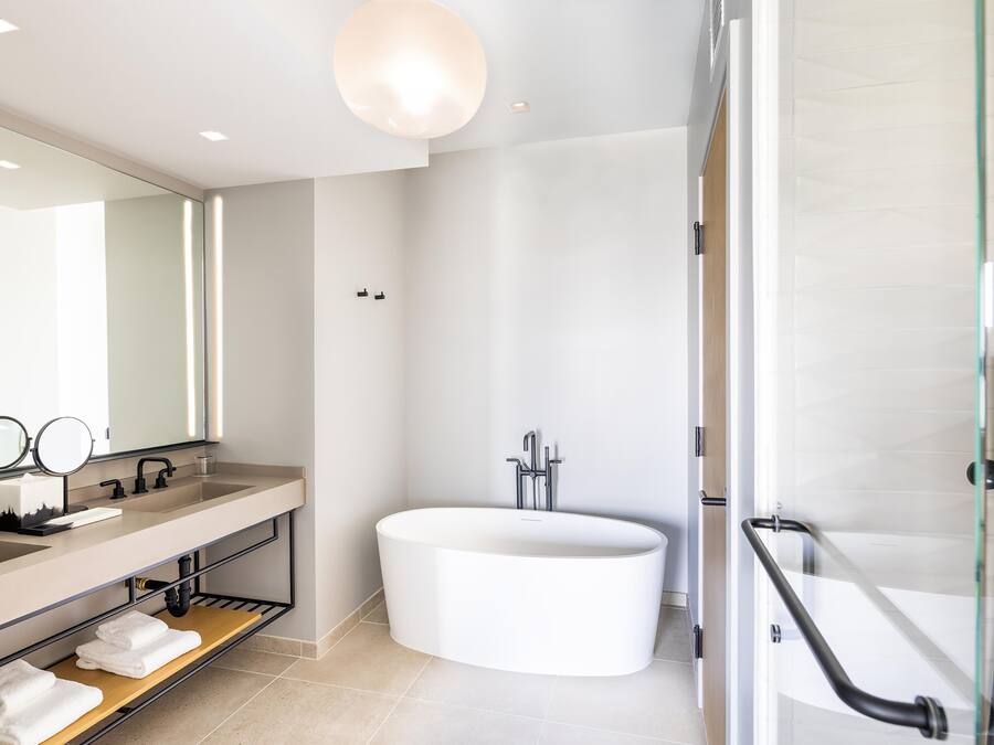Ein modernes Badezimmer mit einer großen Badewanne, einem Waschtisch mit Spiegel und einer Duschkabine aus Glas.