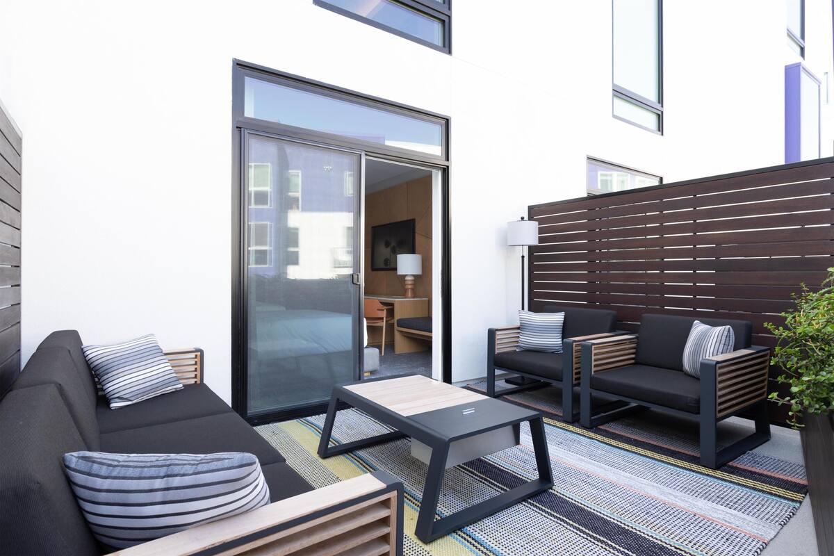 A modern outdoor living area with a sofa, chairs, a table, and a sliding glass door leading to an interior space.