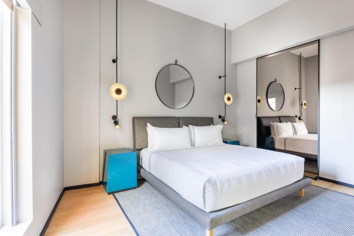 A modern bedroom with a large bed, bedside tables, a mirror, and a view of a bathroom.