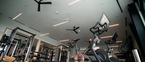 Une salle de sport moderne équipée de ventilateurs de plafond, de vélos d’exercice et d’appareils de musculation.