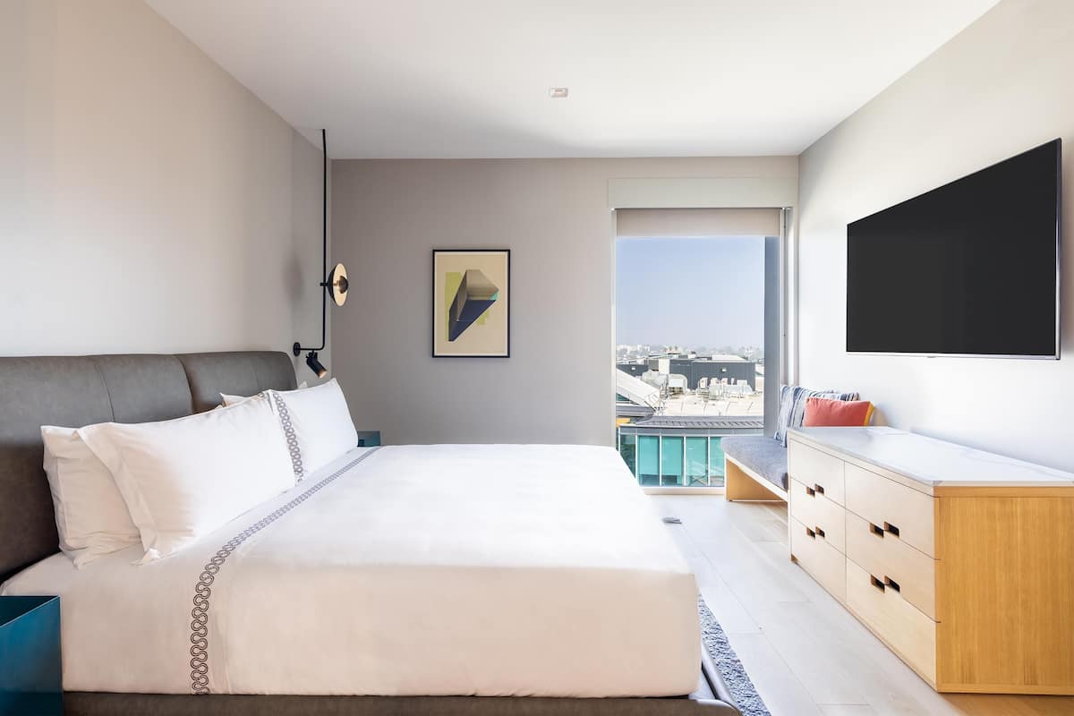 A modern hotel room with a large bed, a TV, a city view, and a balcony.