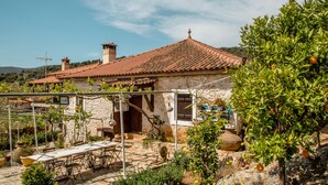Una casa de piedra con techo de tejas, mobiliario exterior y un jardín con árboles cítricos.