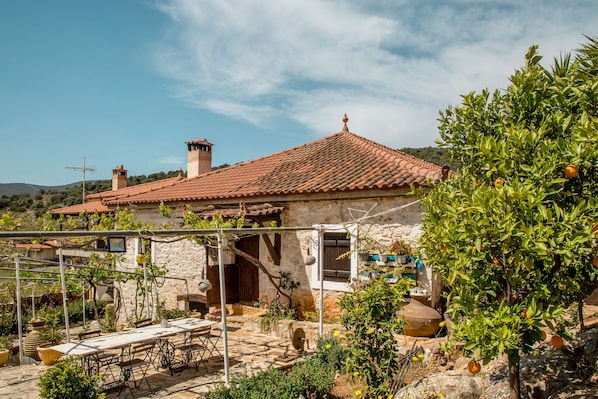 A stone house with a tiled roof, outdoor seating, and a garden with citrus trees.