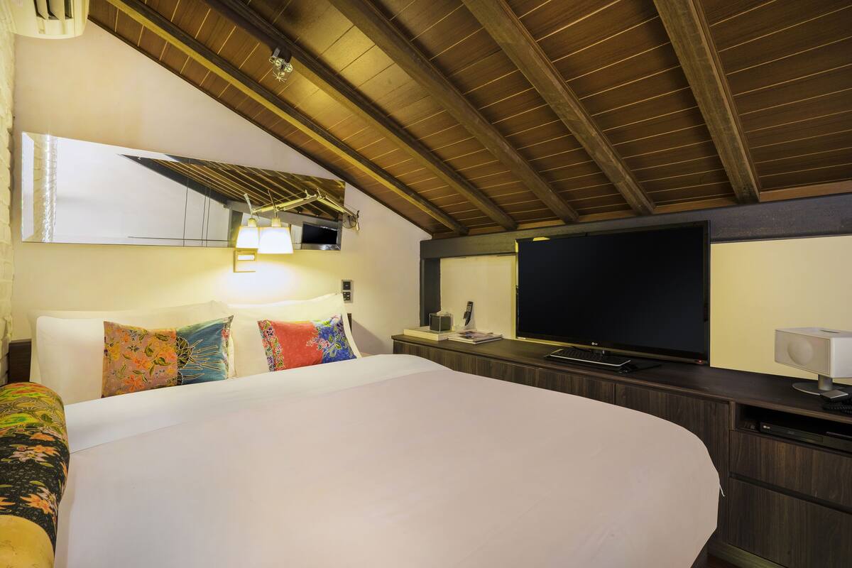 Une chambre d’hôtel avec un grand lit, un téléviseur à écran plat, un bureau avec un ordinateur et un miroir au-dessus du lit.