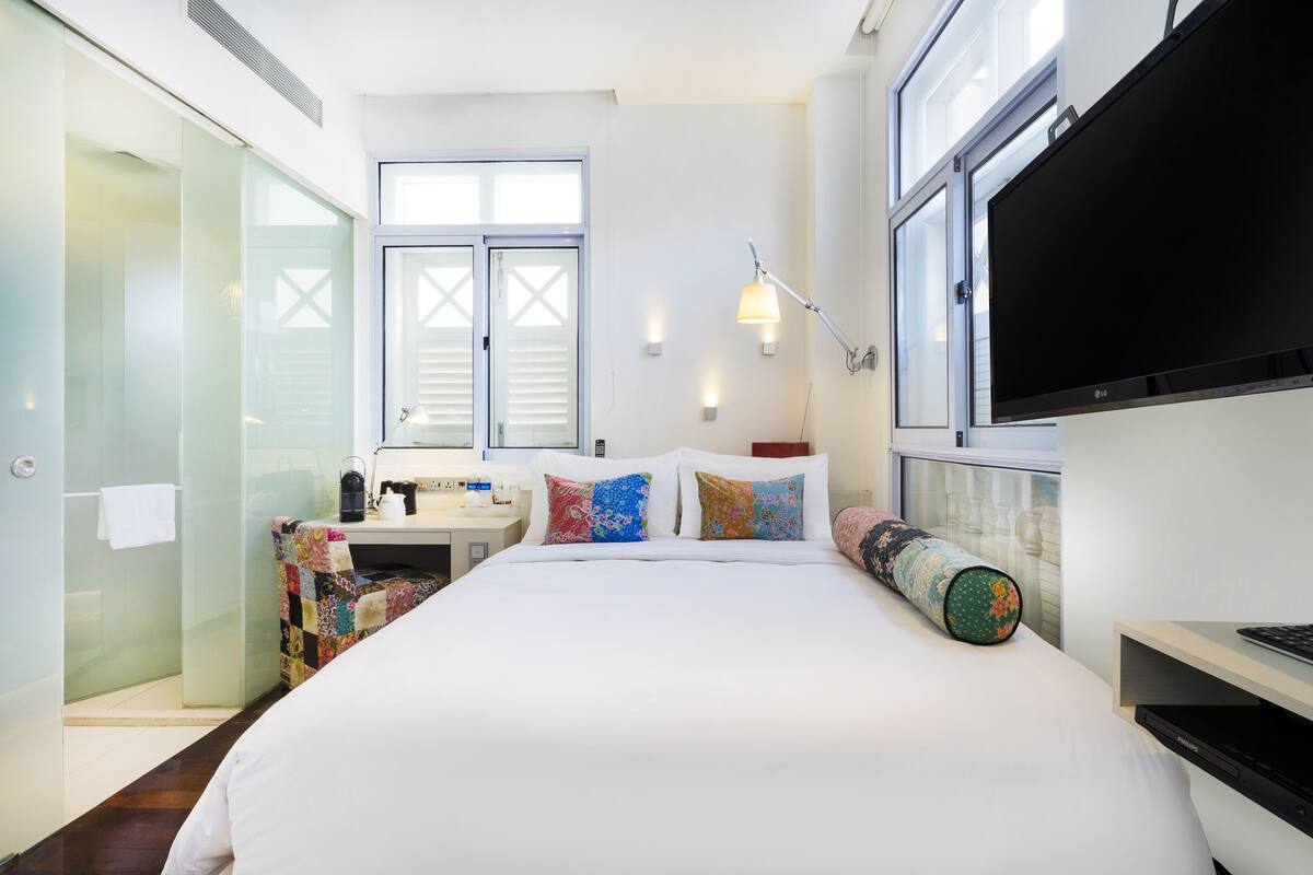 Une chambre d’hôtel moderne dotée d’un grand lit, d’un bureau avec un ordinateur, d’une douche à parois de verre et d’un téléviseur fixé au mur.