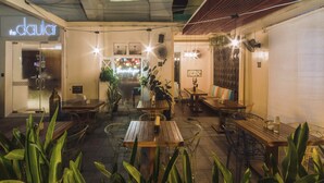 Un espacio de comedor al aire libre con varias mesas y sillas de madera, rodeado de plantas en macetas.