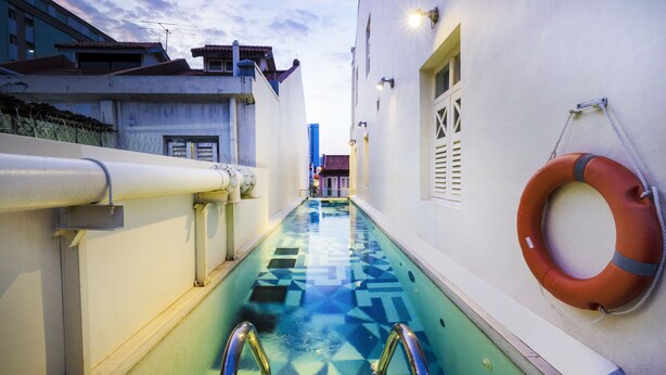 Un área de piscina pequeña con piso de baldosas a cuadros, barandas de metal y un flotador en la pared.