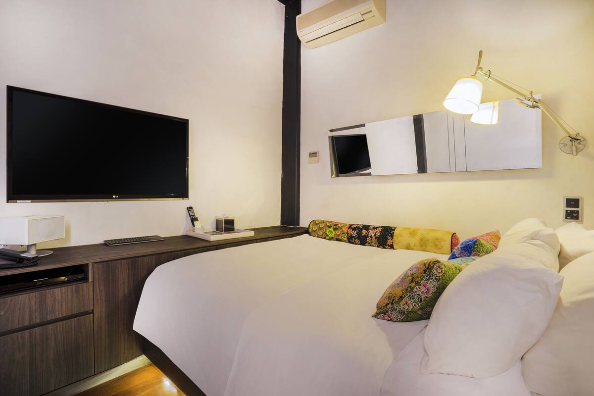 Une chambre d’hôtel dotée d’un grand lit, d’une télévision à écran plat, d’un bureau avec un ordinateur, d’un miroir et d’un climatiseur.