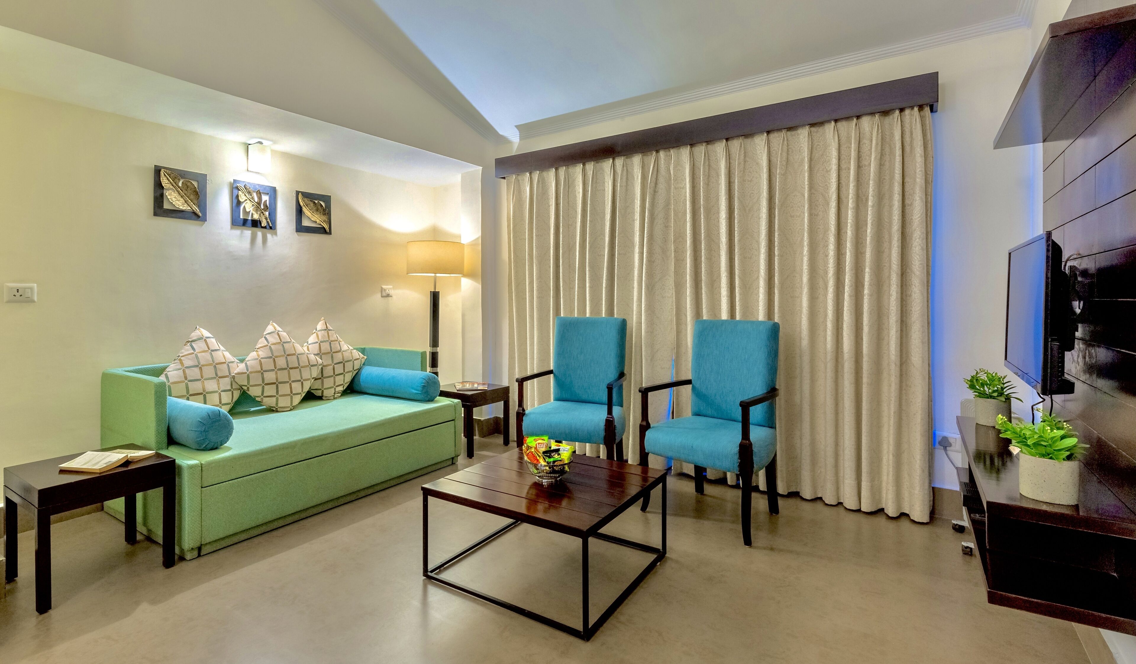 A living room with a green sofa, two blue armchairs, a coffee table, and a TV.