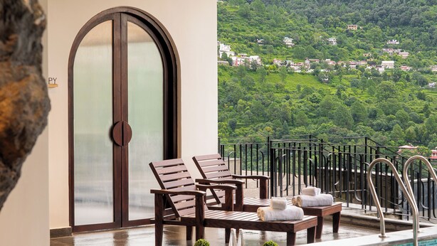 A pool area with lounge chairs, a small table, and a view of a green hillside. - Rosewood Retreat Bhimtal (Nainital)