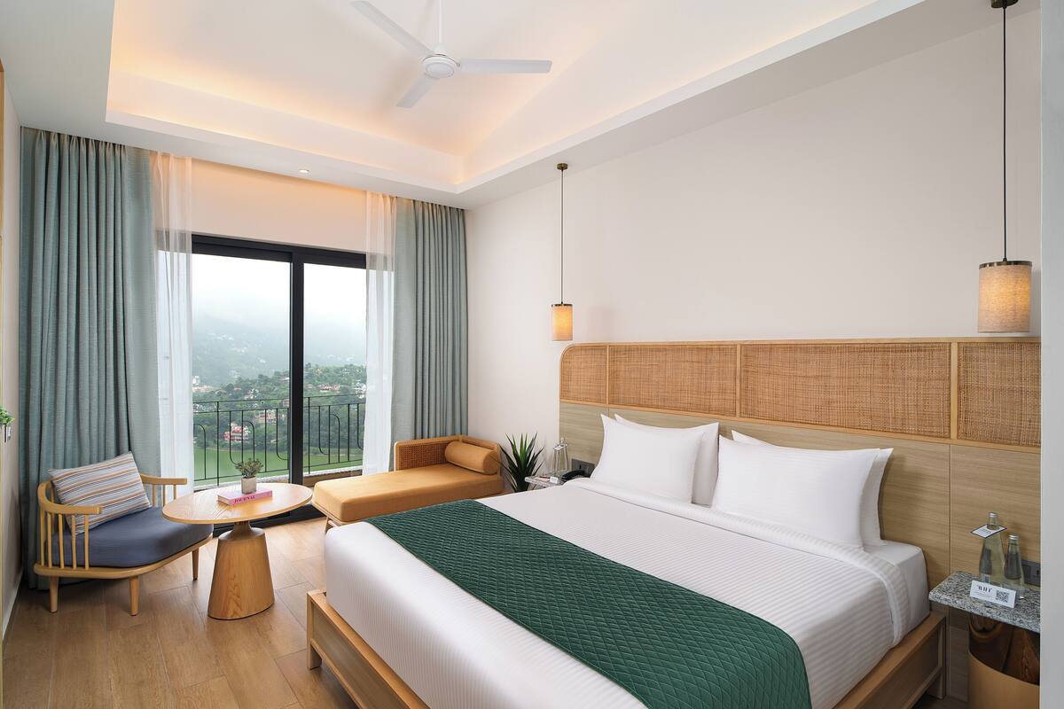 Habitación de hotel con cama, sofá, mesita pequeña, mesita de noche y vistas a la ciudad.