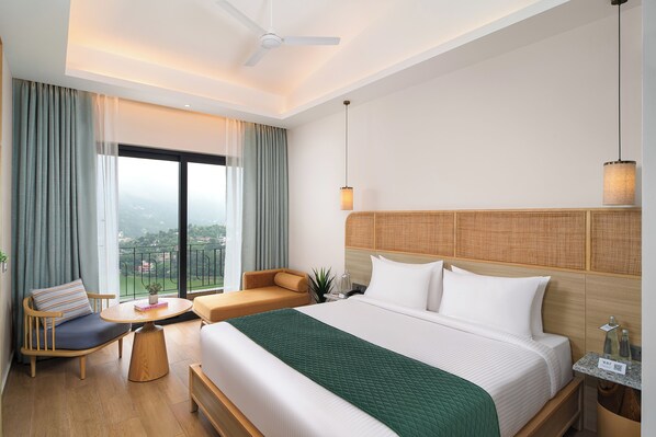 A hotel room with a bed, a sofa, a small table, a nightstand, and a view of the city.