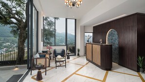 A spacious living area with a large window, a reception desk, and a chandelier. - Rosewood Retreat Bhimtal (Nainital)