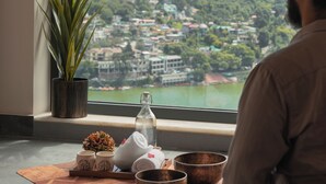 A person sitting by a window with a view of a green hillside and a town below. - Rosewood Retreat Bhimtal (Nainital)