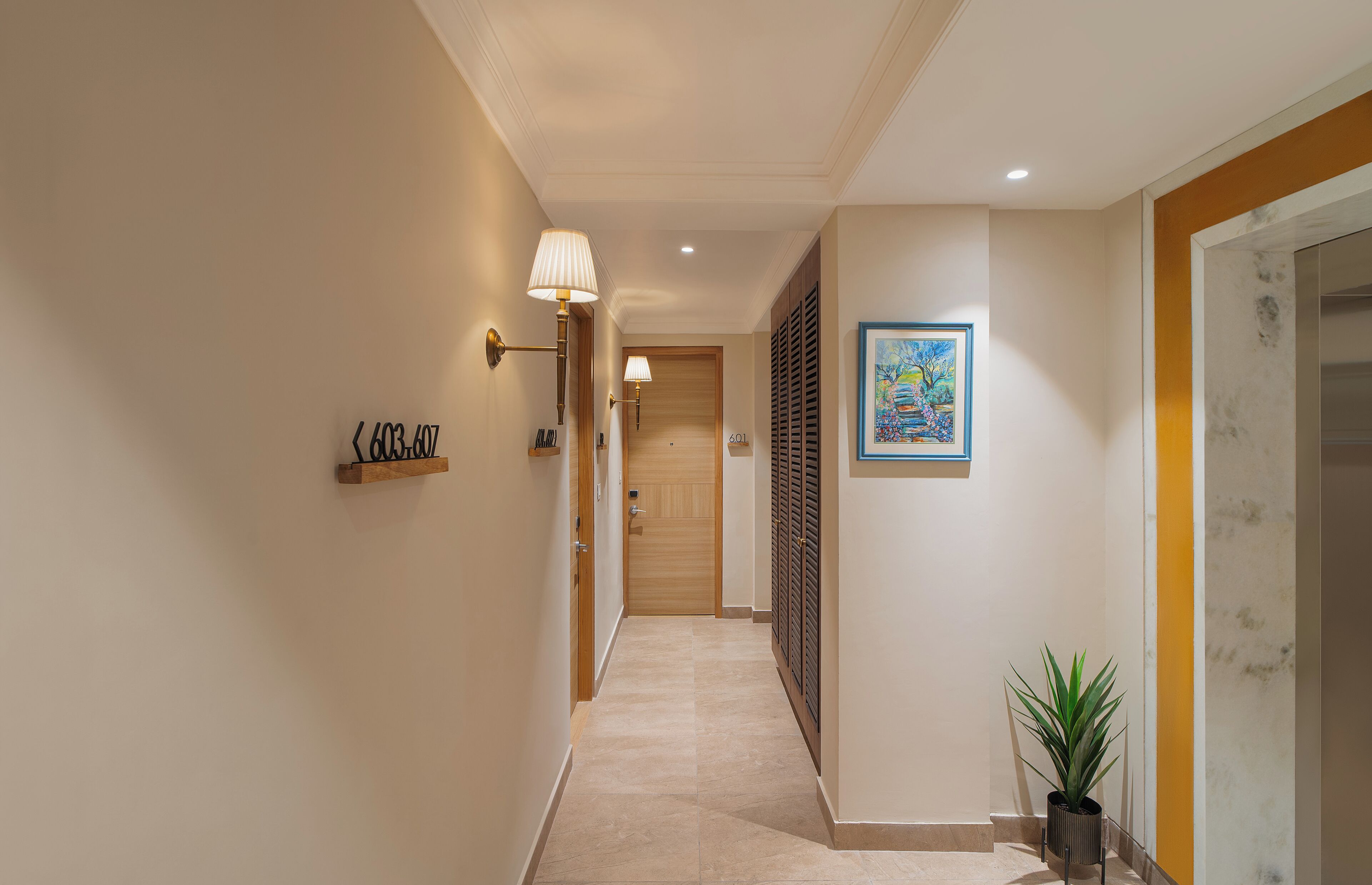 Un pasillo con una puerta de madera al final, una planta en maceta y un cuadro en la pared.