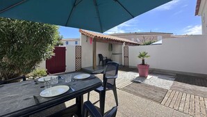 Un patio al aire libre con una mesa preparada para comer, una sombrilla azul y una planta en maceta.