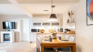 A modern kitchen with white cabinets, a wooden dining table, and a TV mounted on the wall. - Apartment Seebrücke in the Ostseebad Wustrow (Ostseebad Wustrow)