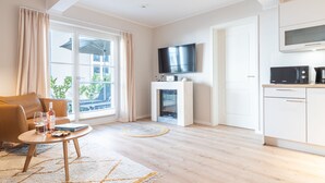A modern living room with a sofa, a coffee table, a fireplace, a TV, and a kitchen area. - Apartment Seebrücke in the Ostseebad Wustrow (Ostseebad Wustrow)