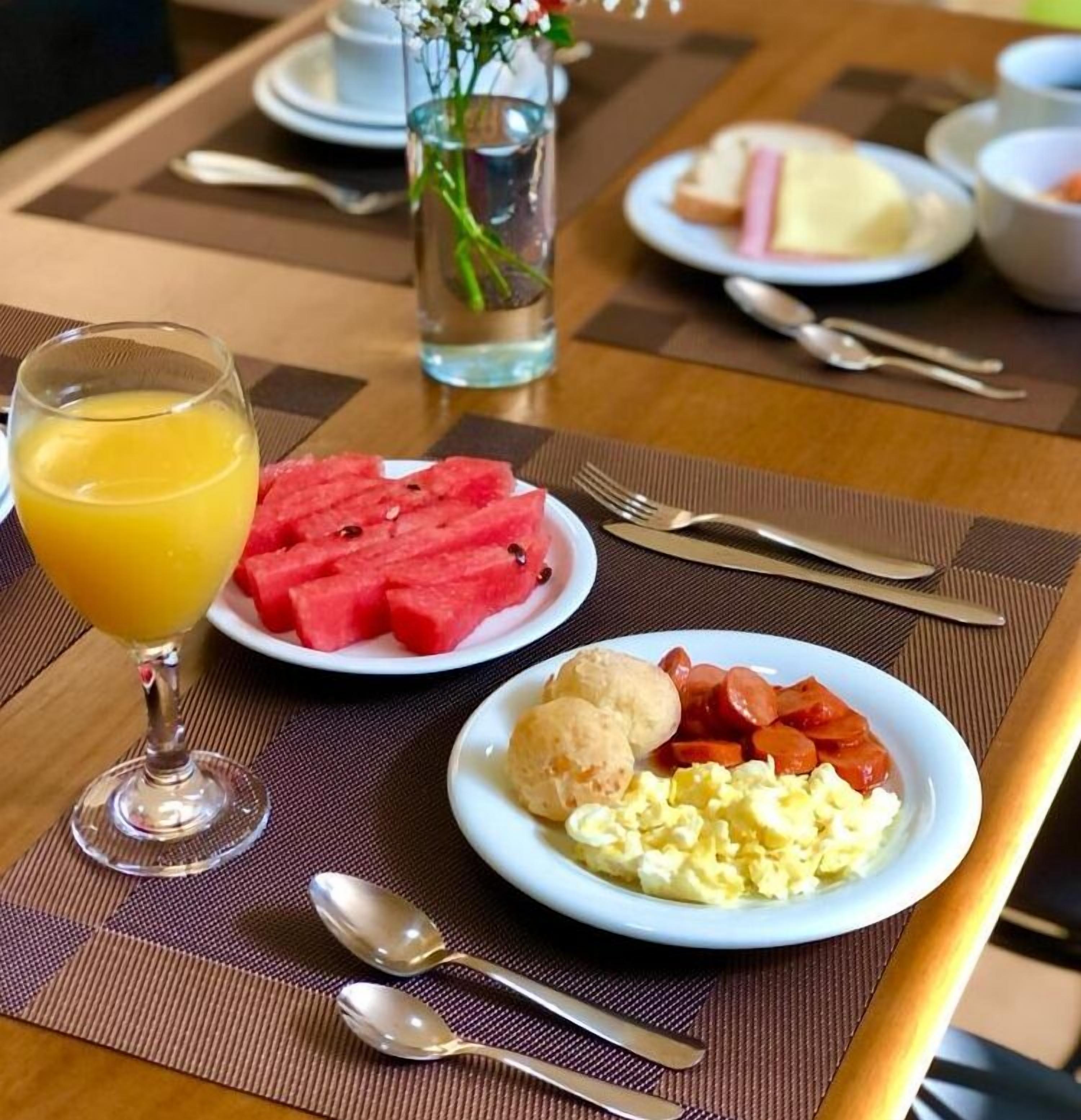 Un desayuno con platillos de sandía, huevos revueltos, salchicha y tostadas.