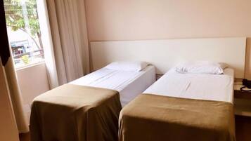Quarto de hotel com duas camas de solteiro, uma janela com cortinas e uma mesinha com telefone.