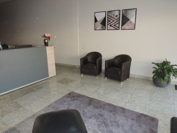 Zona de recepción con mostrador, dos sillones, planta en maceta y arte abstracto en la pared.