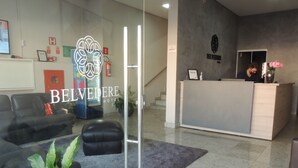 A hotel reception area with a modern design, including a reception desk, seating area with sofas, and potted plants. - Hotel Belvedere Araras - Fácil Acesso Hospital São Leopoldo e Faculdades (Araras)