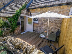 A stone building with a wooden deck, a glass door, and a table with chairs. - Sea Pink Cottage (Swanage)