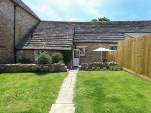 A stone building with a tiled roof, a stone pathway leading to a door, and a wooden fence enclosing a grassy yard. - Sea Pink Cottage (Swanage)