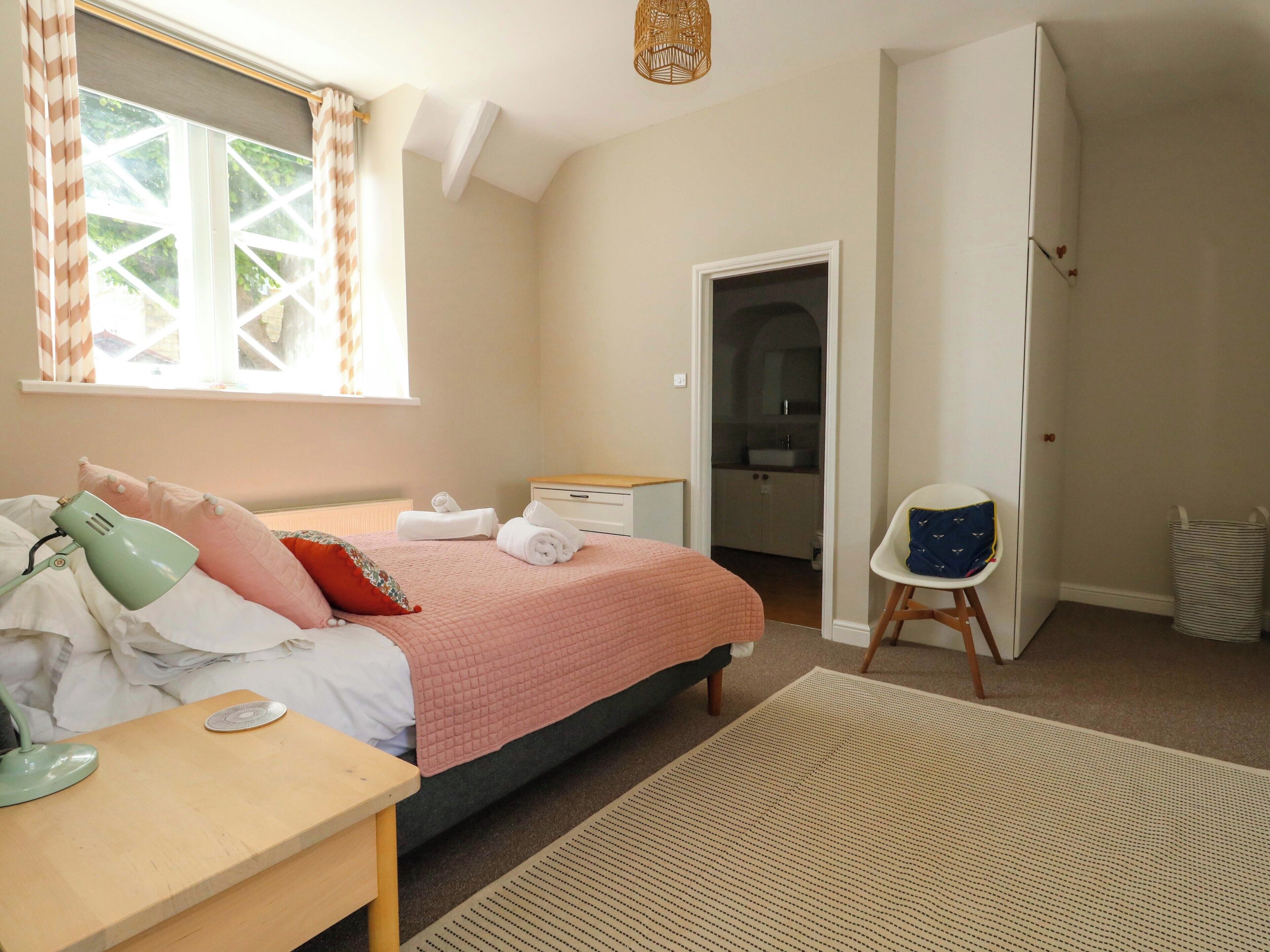 A bedroom with a bed, bedside table, lamp, and a view of the bathroom.