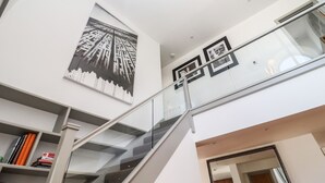 Un interior moderno con una escalera, un cuadro grande de un paisaje urbano en blanco y negro, y fotografías enmarcadas en las paredes.