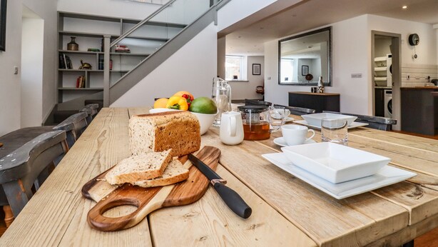 Una cocina moderna con una mesa de madera, una tabla de cortar con pan y un hervidor.