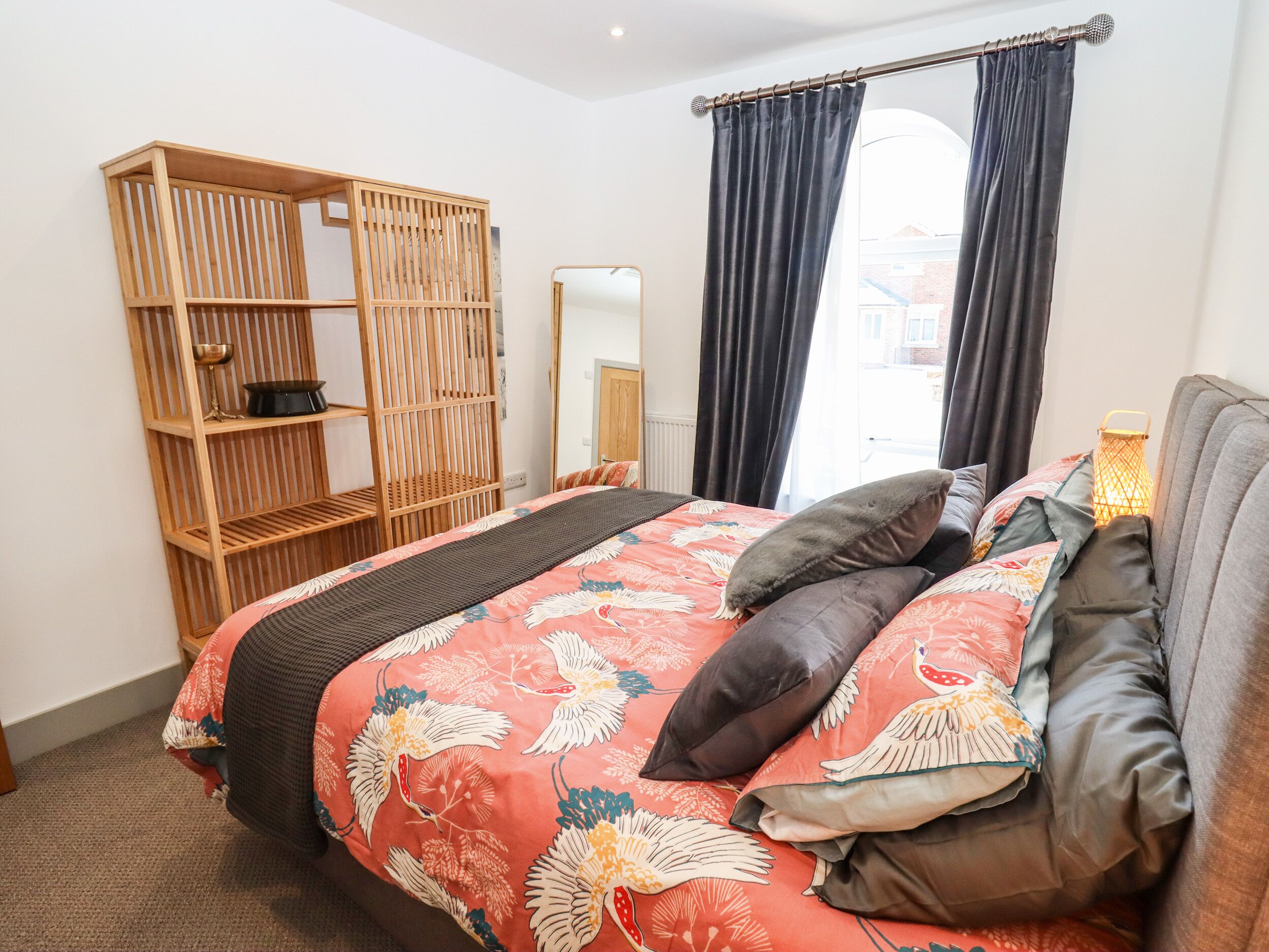 Ein Schlafzimmer mit einem Bett, einem Holzschrank, einem Spiegel und einem Fenster mit Vorhängen.