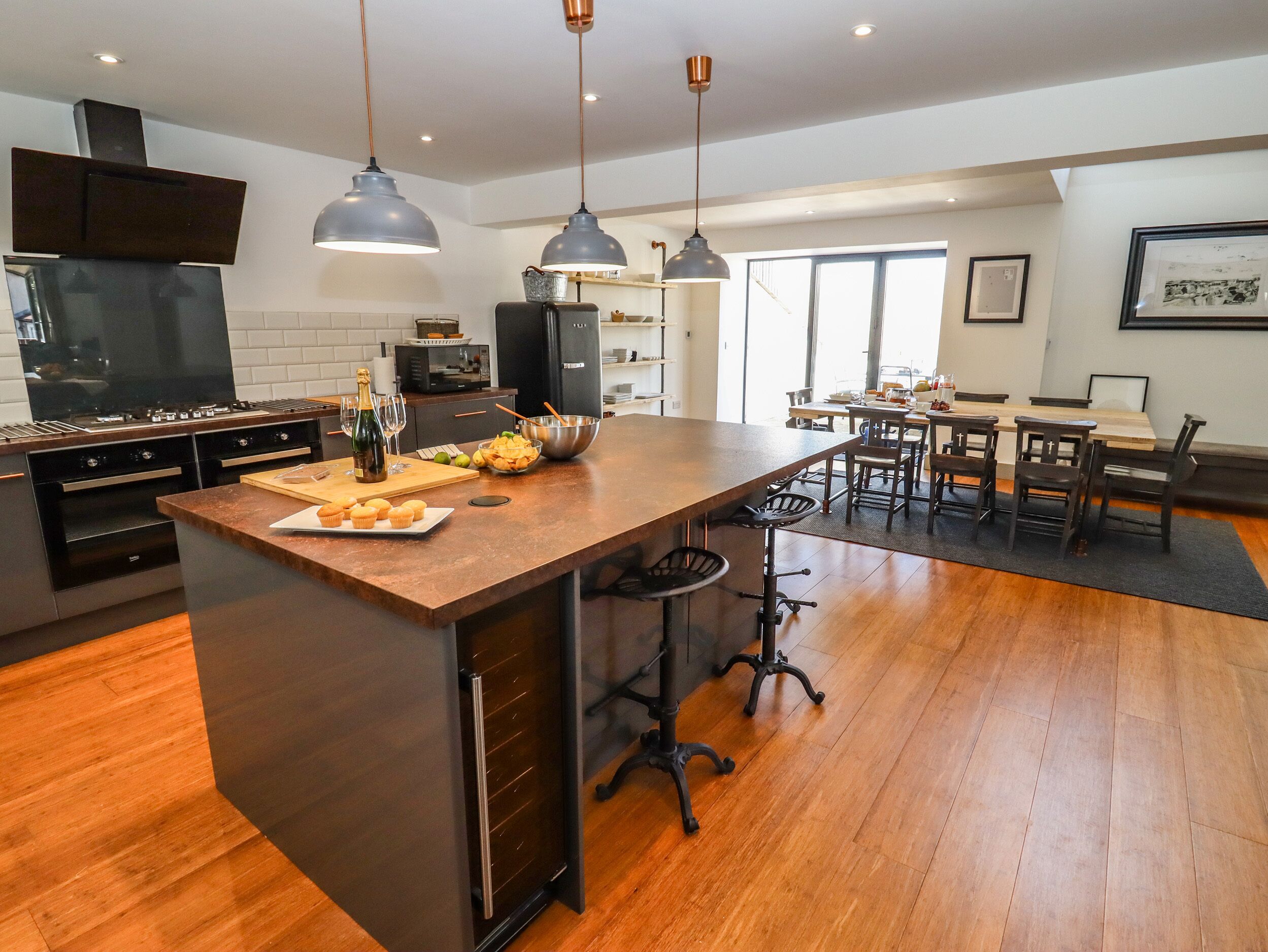 A modern kitchen with a central island, stainless steel appliances, pendant lighting, and a dining area with wooden furniture.