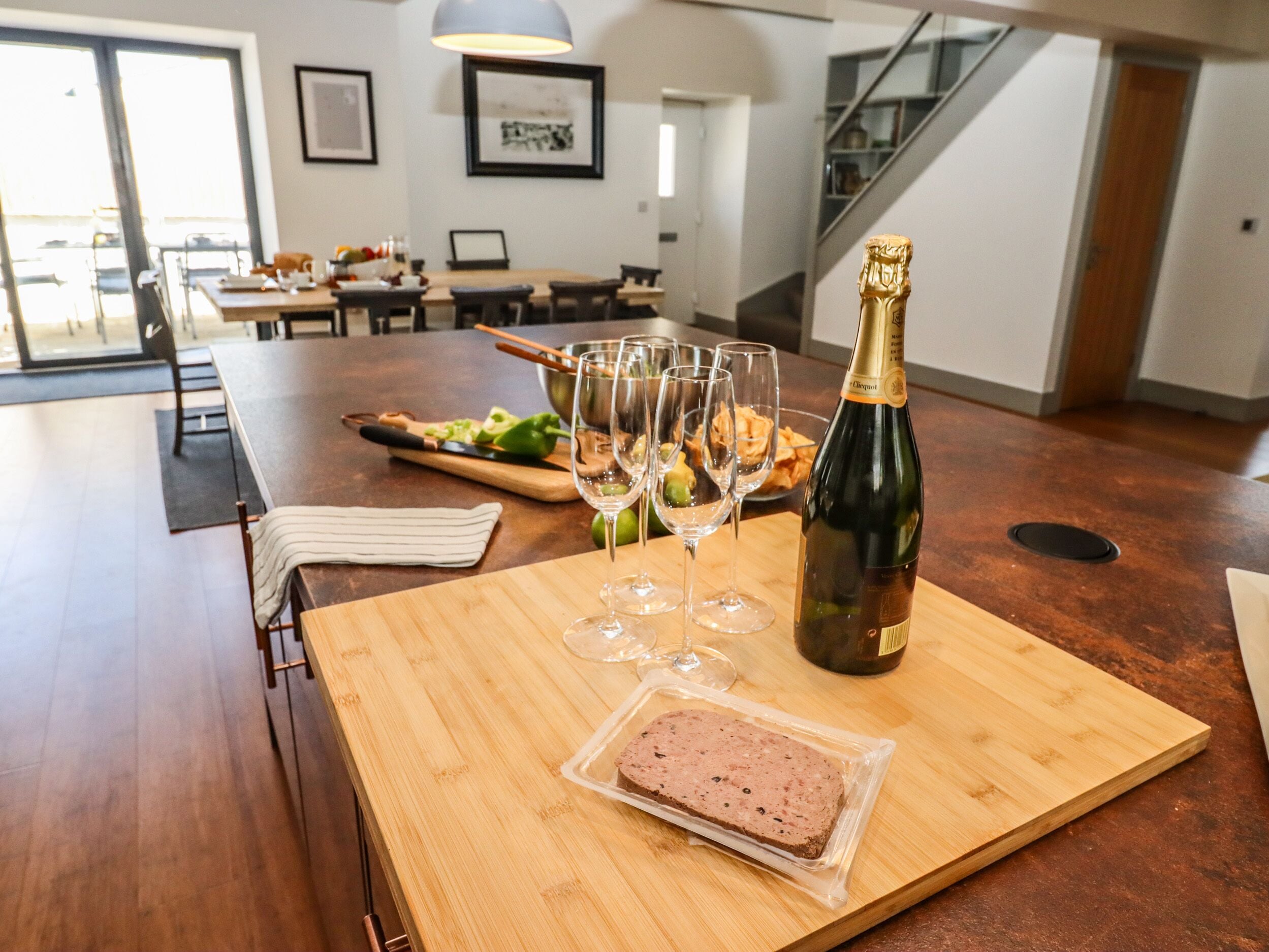 Een houten eettafel met een champagnefles, verschillende wijnglazen en een verpakt vleesgerecht.