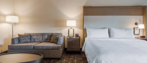 A hotel room with a bed, a sofa, a nightstand, a lamp, and a small round table.