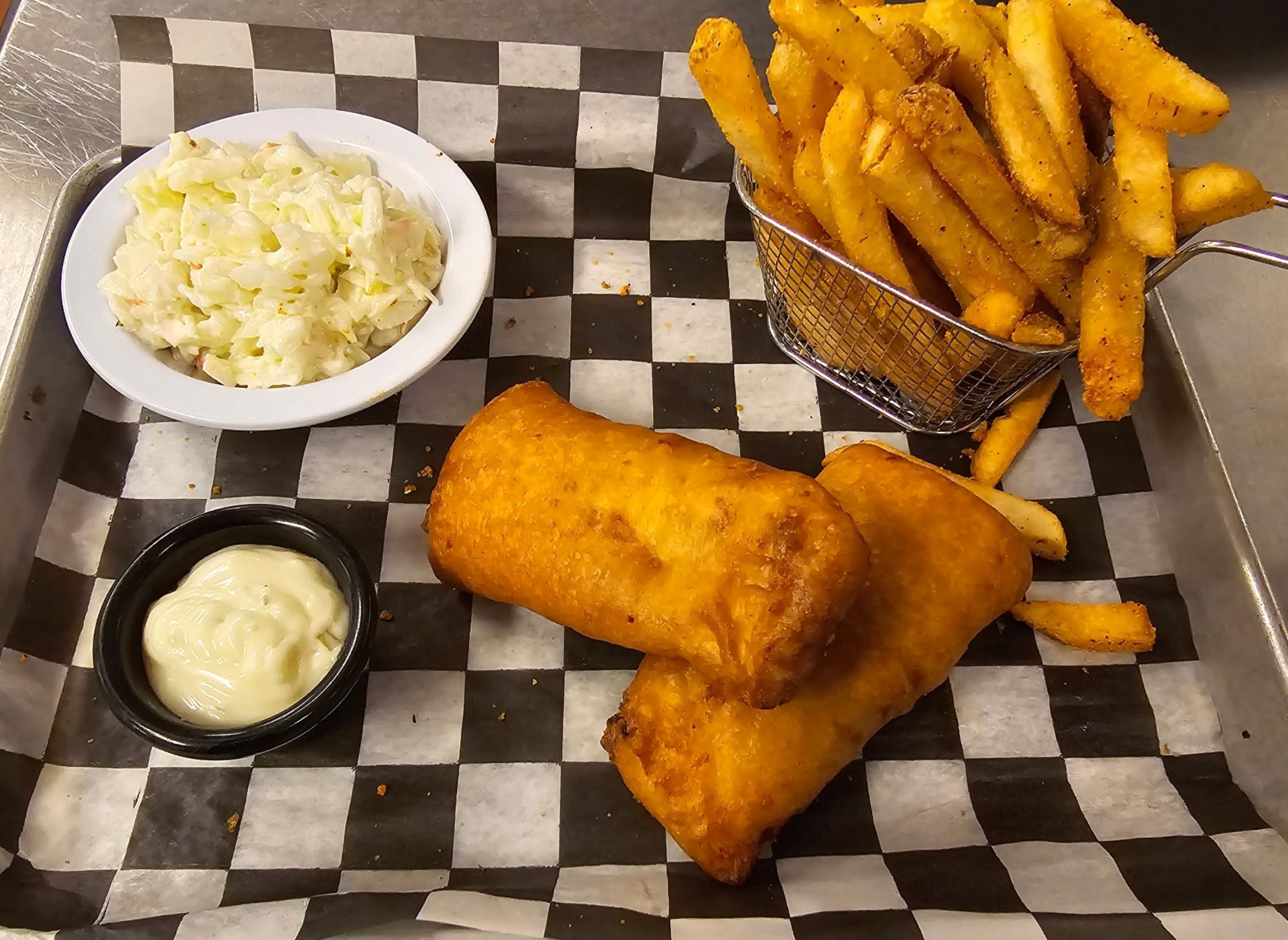 Een schaal met fish and chips, een klein kommetje mushy peas, en een bakje tartare saus.