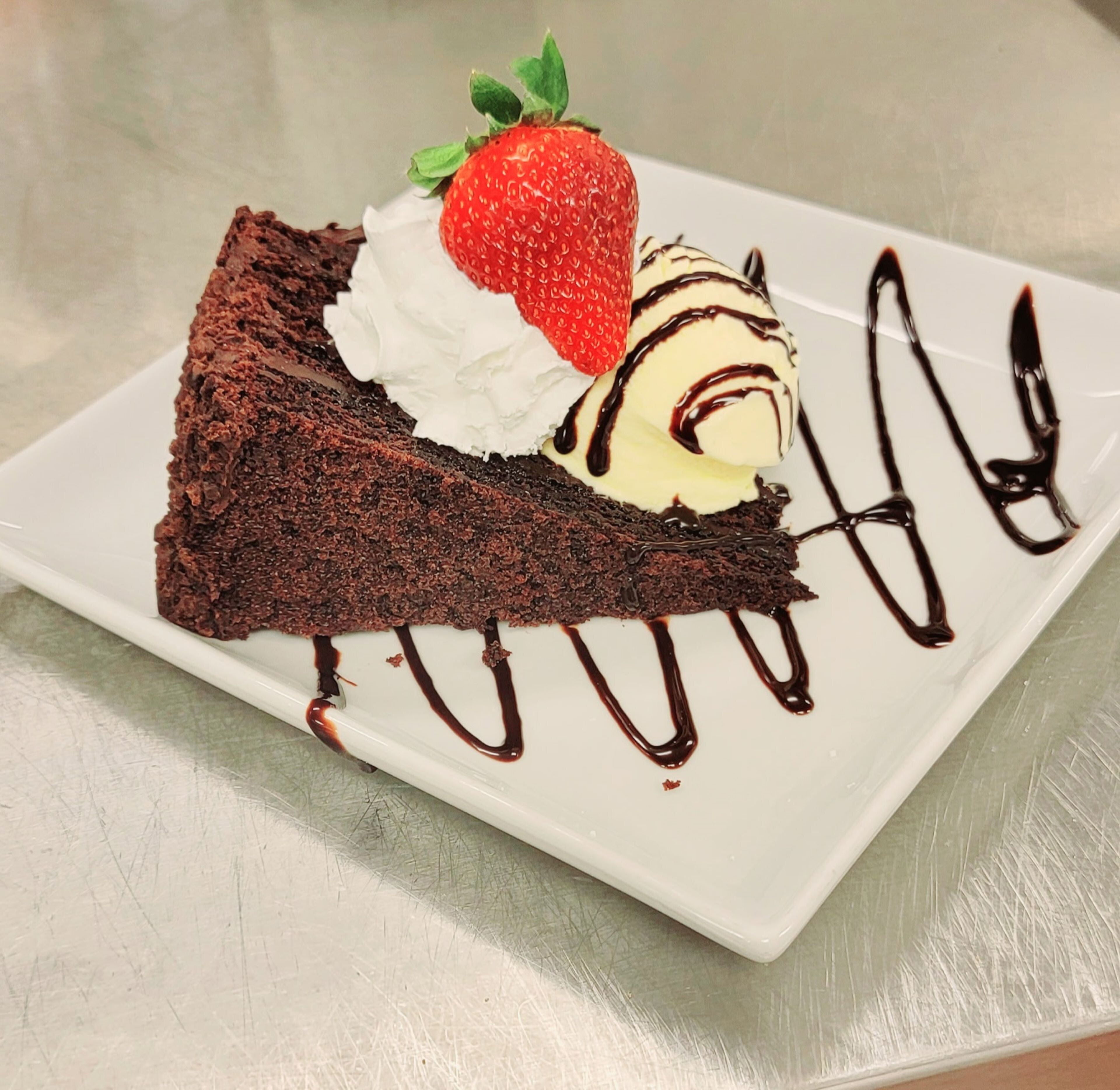 A slice of chocolate cake with whipped cream and a strawberry on a white plate.