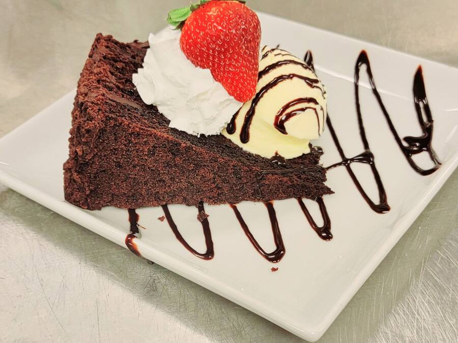 A slice of chocolate cake with whipped cream and a strawberry on a white plate.
