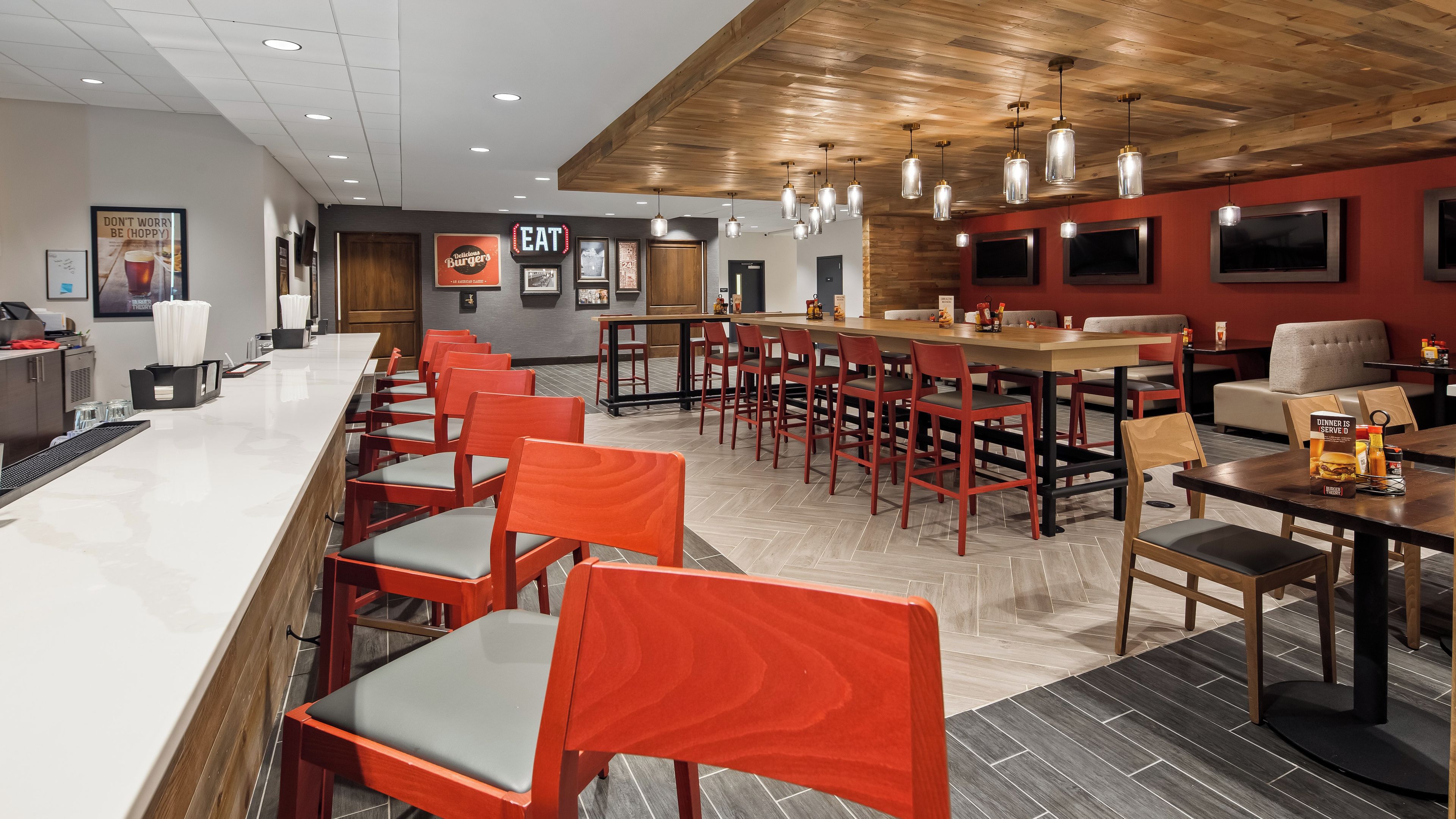 A restaurant with a bar area, multiple dining tables, and red chairs.