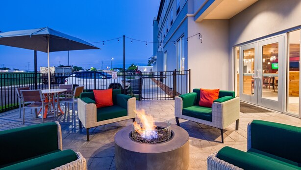 An outdoor patio with wicker furniture, a fire pit, and a view of the street and buildings in the background. - Holiday Inn Clarksville Northeast by IHG (Clarksville)