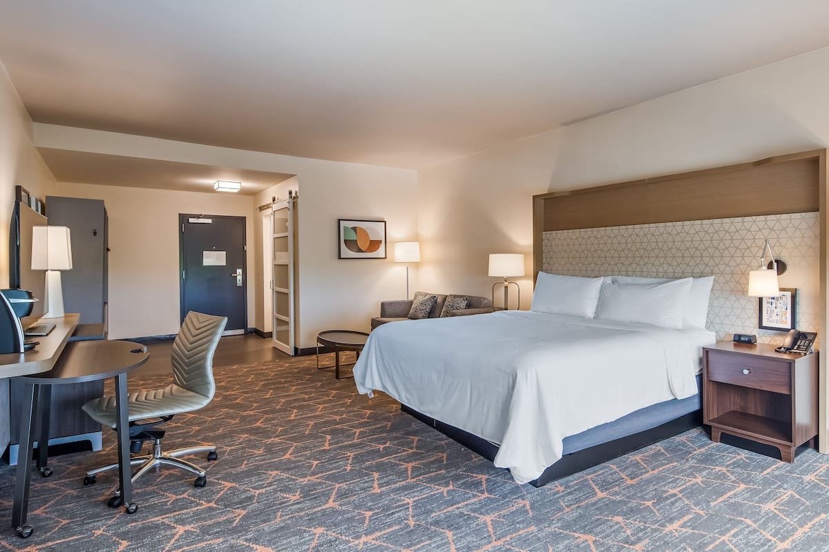 Una habitación de hotel con cama, escritorio, silla y dos mesitas de noche con lámparas.