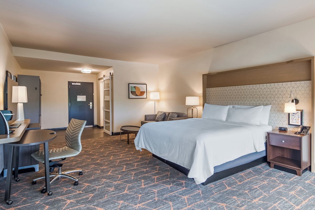 Quarto de hotel com cama, escrivaninha, cadeira e duas mesas de cabeceira com abajures.